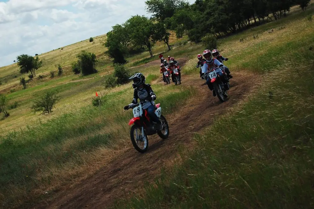 Children riding Honda dirt bikes on winding country trail at Iron Horse Country Ranch Summer Camp, Austin Texas