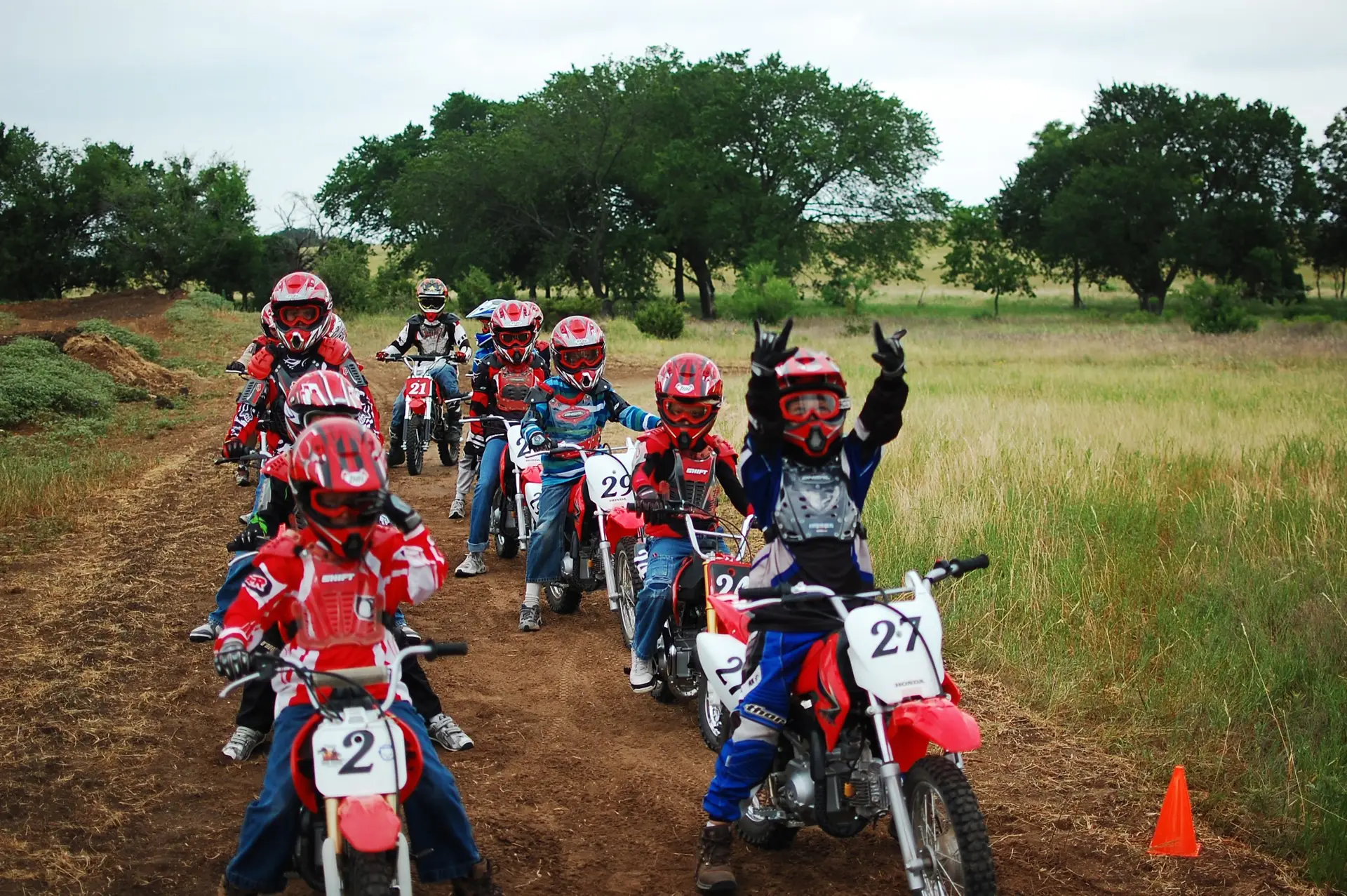 Kids on motocross bikes riding on Honda Crf 70 and 110 motorcycles saluting camera ready to ride track at Summer Camp