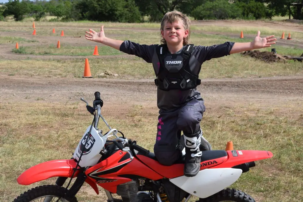 smiling boy motocross rider kneeling on Honda dirt bike with arms wide open